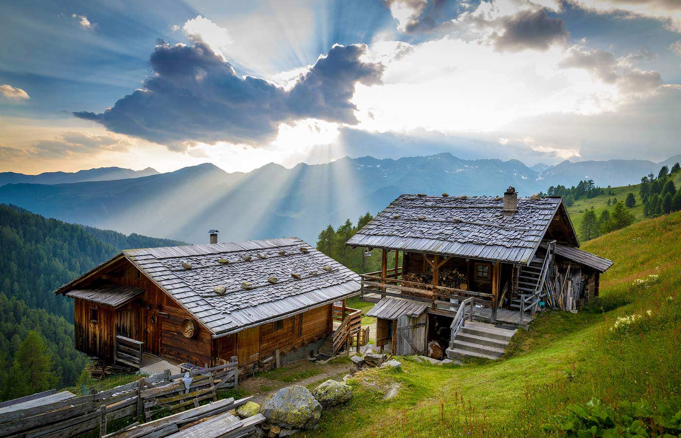 Two old wooden alpine huts illuminated by the light of the sun hidden by the clouds